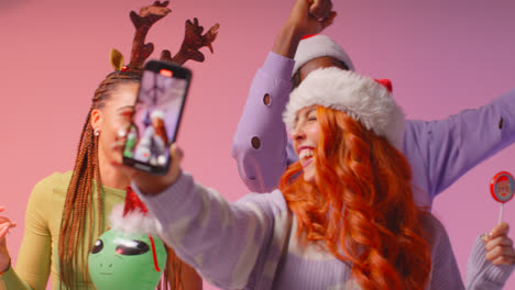 Studio-Shot-Of-Gen-Z-Friends-Dancing-And-Posing-For-Selfie-At-Christmas-Party-Wearing-Santa-Hat-And-Reindeer-Antlers-2